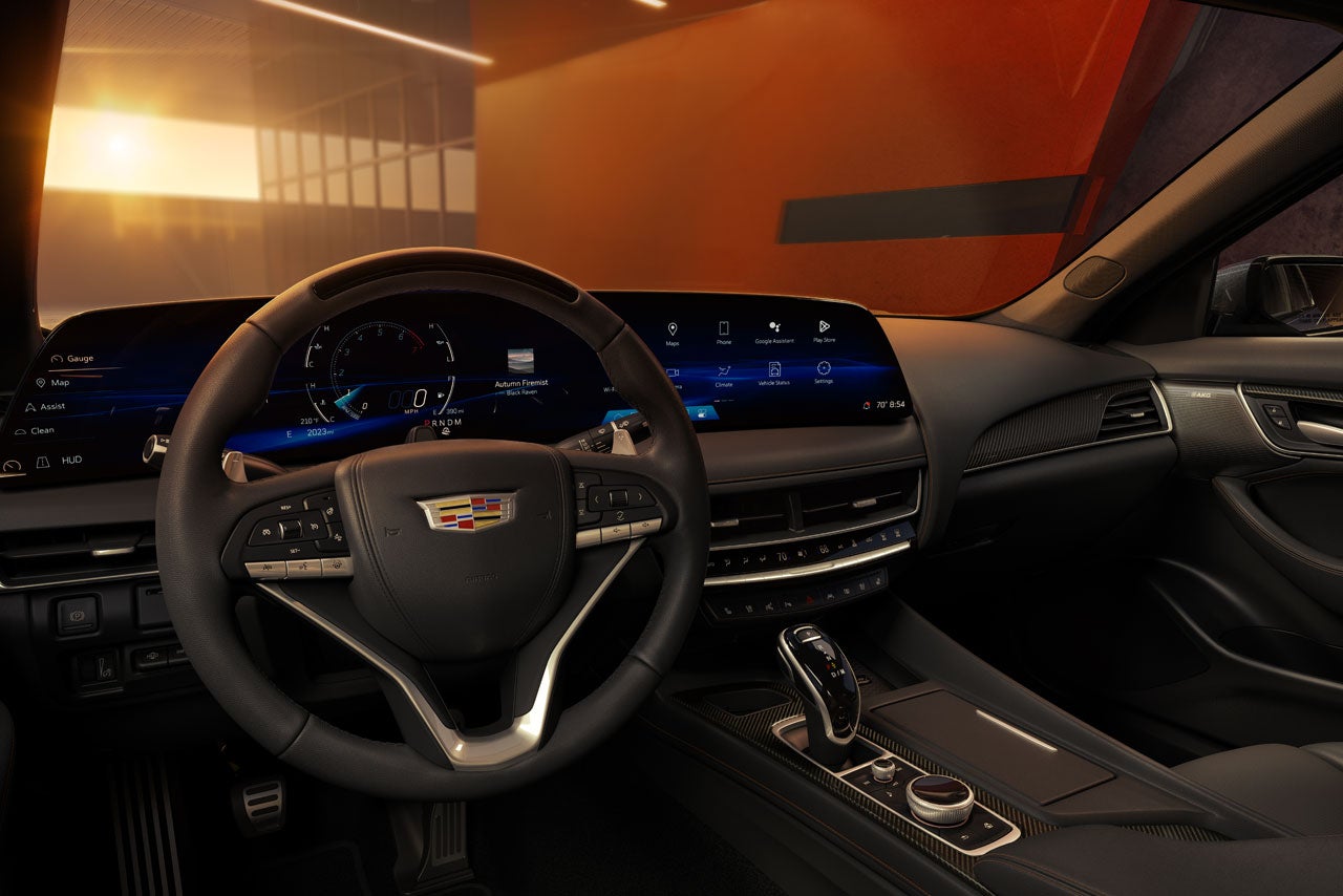 Interior of a modern car, showing the steering wheel, large digital dashboard, and center console, with a warm sunset visible through the windshield.